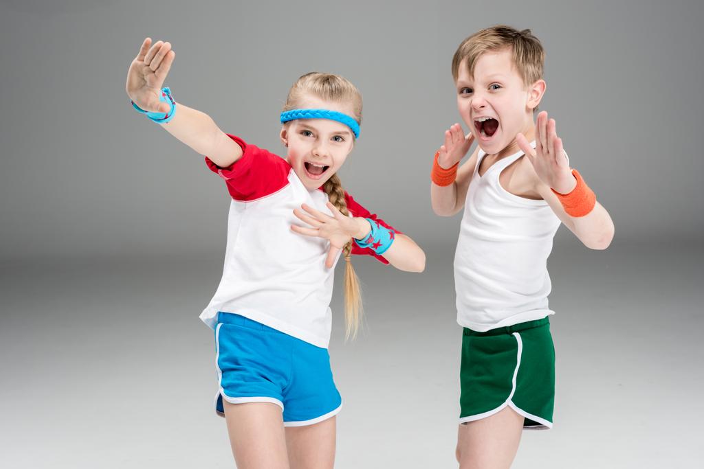 子供スポーツ コンセプトのスポーティな男の子と女の子スポーツウェアを行使し グレーに分離された身振りで示すことに ロイヤリティフリー写真 画像素材