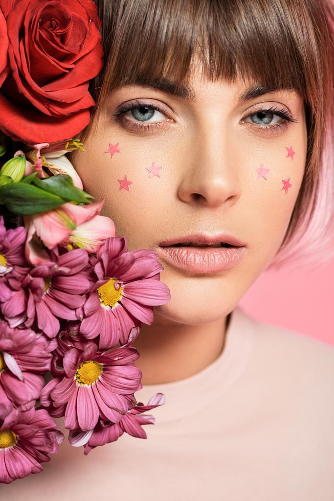 彼女の顔を彼女の顔に近い明るい花を持つポーズとカメラ目線につ星の評価を持つ若い女性 ロイヤリティフリー写真 画像素材