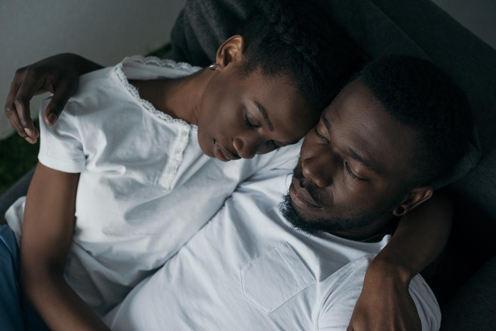 自宅のソファーに寝ながら抱きしめる美しい若いアフリカ系アメリカ人カップル ロイヤリティフリー写真 画像素材