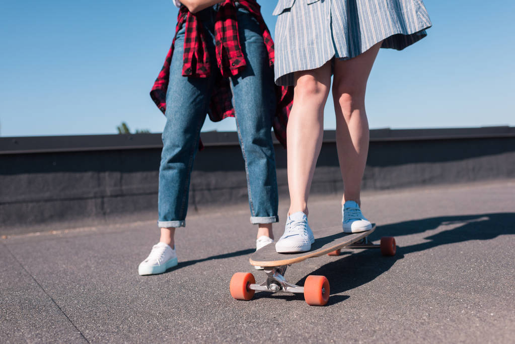 スケート ボードに乗って彼女の女友達を教える女性のショットをトリミング ロイヤリティフリー写真 画像素材