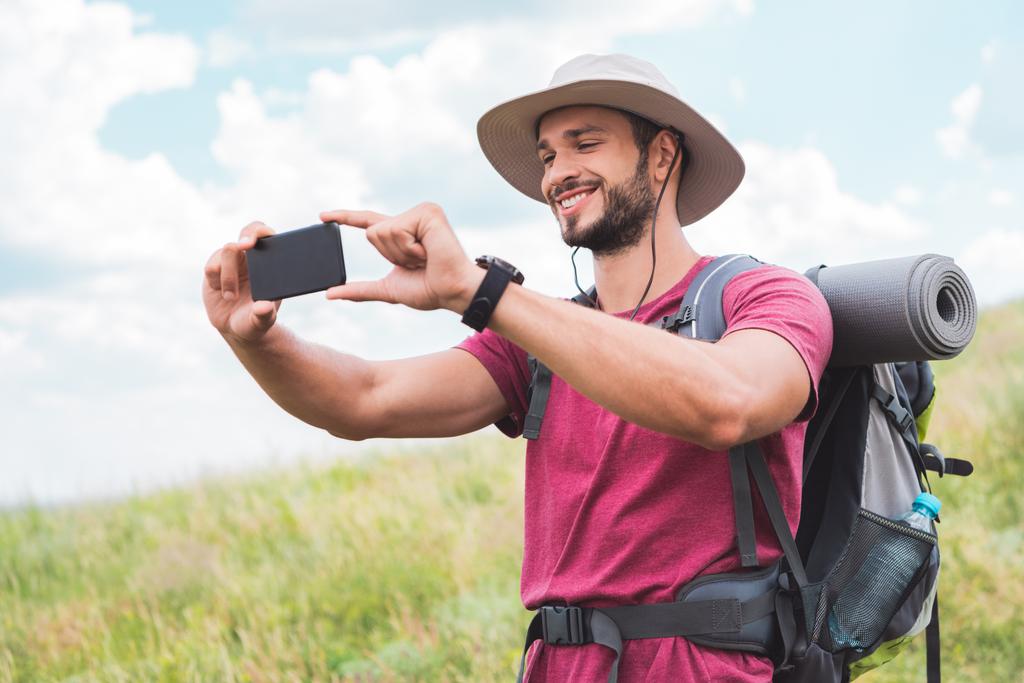 夏の草原にスマート フォンで写真を撮るバックパックで旅行者 ロイヤリティフリー写真 画像素材