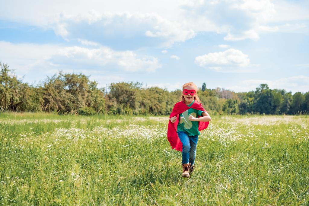 赤いスーパー ヒーロー マントとマスク夏の日に草原の中で幸せな子供 ロイヤリティフリー写真 画像素材