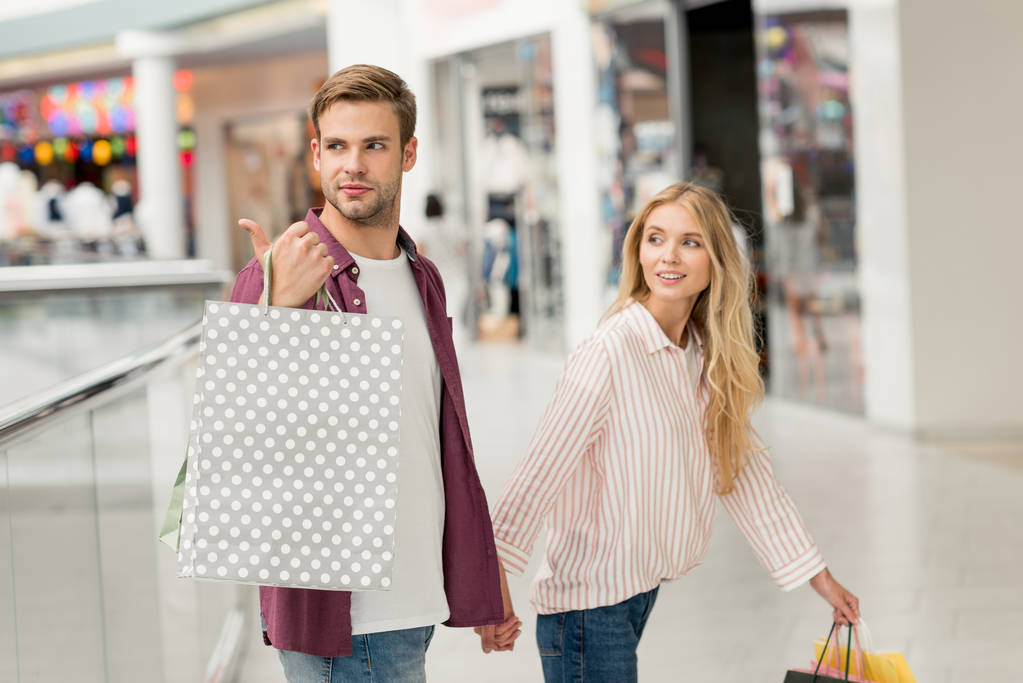 ショッピング モールに近くを歩いてのガール フレンドを指で指すの買い物袋を持った若い男 ロイヤリティフリー写真 画像素材