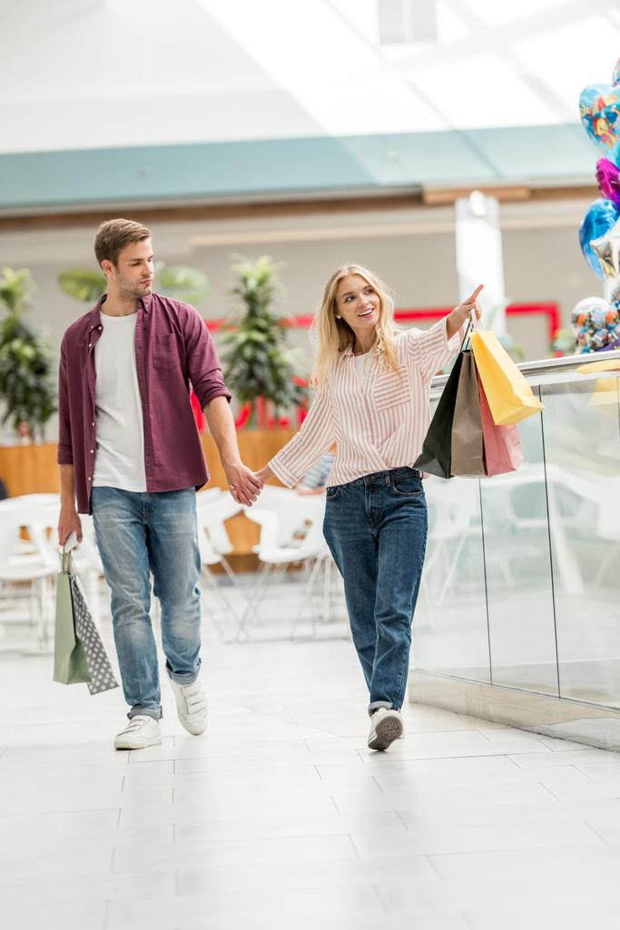 ショッピング バッグのショッピング モールに近く歩く彼氏を指していると美しい若い女性 ロイヤリティフリー写真 画像素材