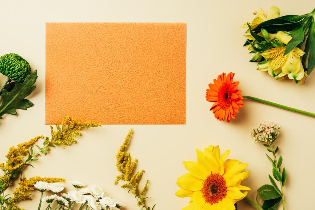 ベージュの背景の空のオレンジ カードの周りの様々 な野生の花とフラット レイアウト ロイヤリティフリー写真 画像素材