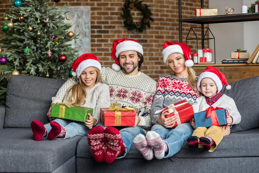 クリスマス プレゼントを押し 家で一緒に座っているサンタ帽子で幸せな家族 ロイヤリティフリー写真 画像素材