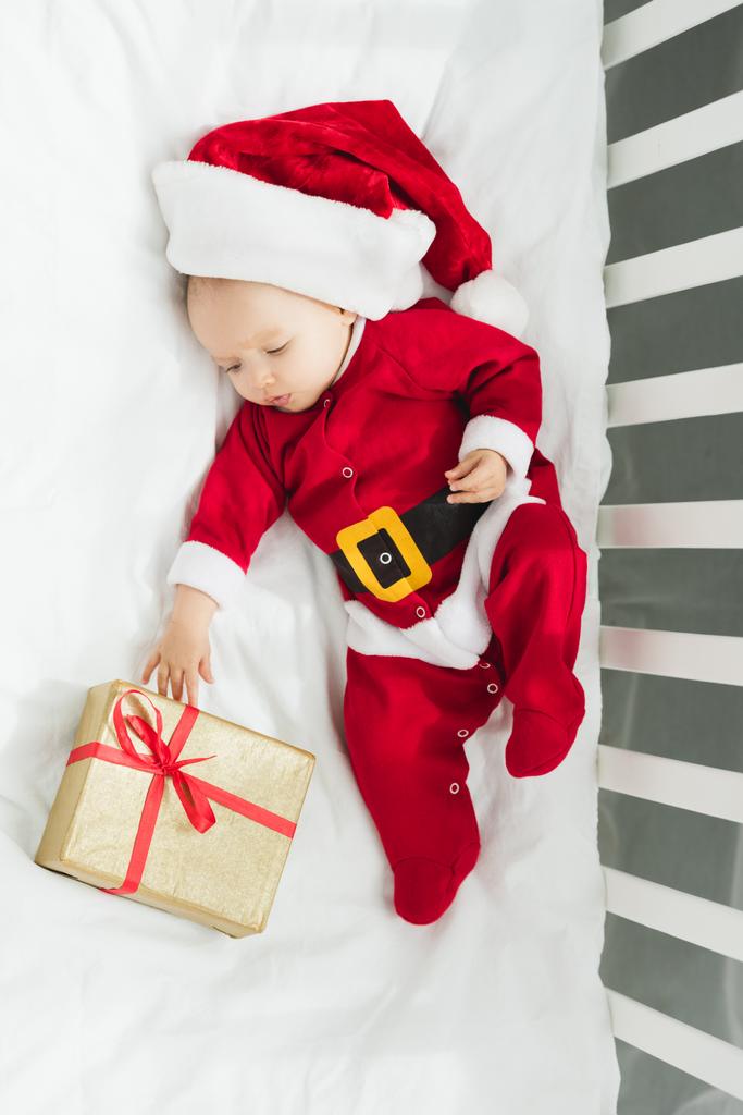 サンタ服クリスマス プレゼント付きのベビーベッドに横たわっているで美しい小さな赤ちゃんの平面図 ロイヤリティフリー写真 画像素材
