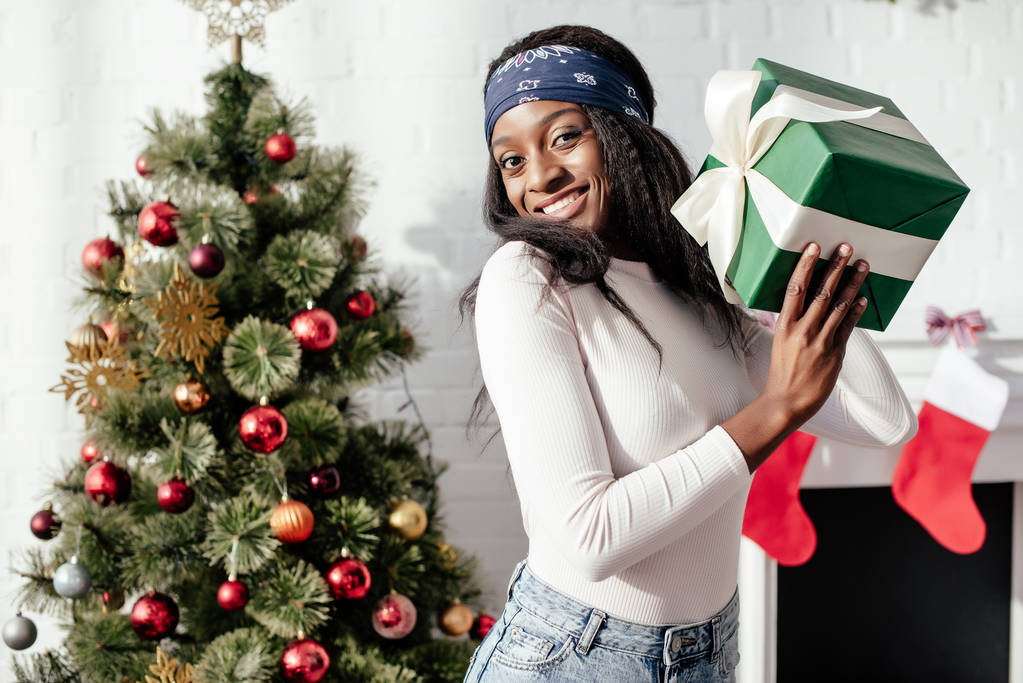 美しい幸せなアフリカ系アメリカ人の女性家でクリスマス プレゼントを抱えて カメラ目線 ロイヤリティフリー写真 画像素材