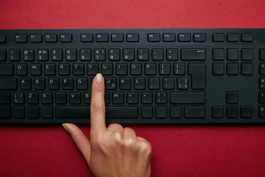 赤の背景に黒のコンピューター キーボード ボタンを押す女性のビューをトリミング ロイヤリティフリー写真 画像素材