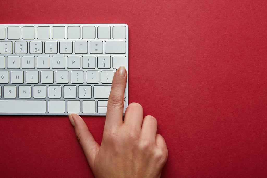 赤の背景にコンピューターのキーボードでボタンを押す女性のビューをトリミング ロイヤリティフリー写真 画像素材