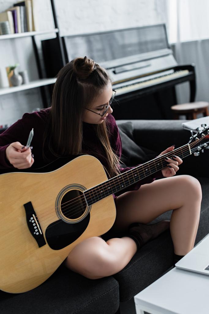 女の子のソファに座って ギターを弾いて マリファナをリビング ルームで共同開催 ロイヤリティフリー写真 画像素材
