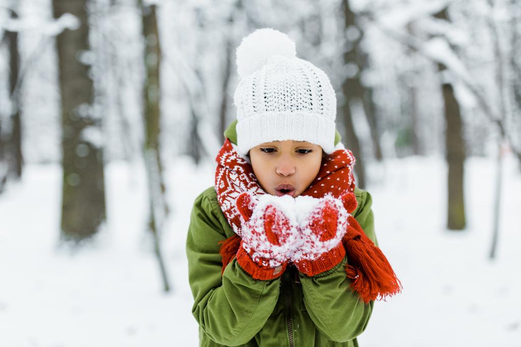 冬の森の雪を吹くかわいいアフリカ系アメリカ人の子 ロイヤリティフリー写真 画像素材