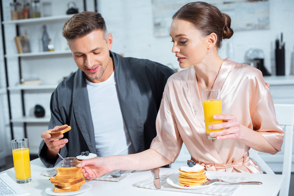 夫と妻のパンケーキの朝食中にローブとキッチンでオレンジ ジュースの選択と集中 ロイヤリティフリー写真 画像素材