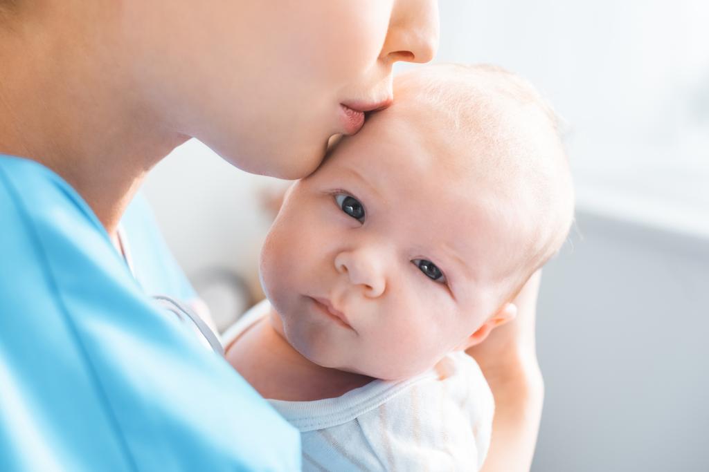 若い母親はカメラ目線かわいい赤ちゃんにキスのショットをトリミング ロイヤリティフリー写真 画像素材