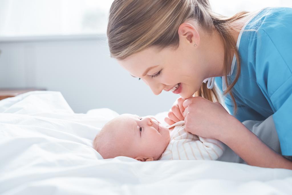 病室でかわいい赤ちゃんの手を取り合って幸せな若い母の側面図 ロイヤリティフリー写真 画像素材