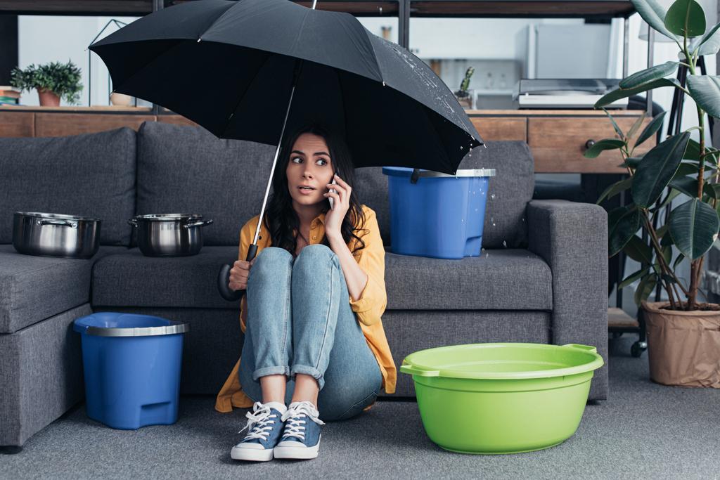 スマート フォンで話して 傘付きのリビング ルームに座っているジーンズの女の子 ロイヤリティフリー写真 画像素材