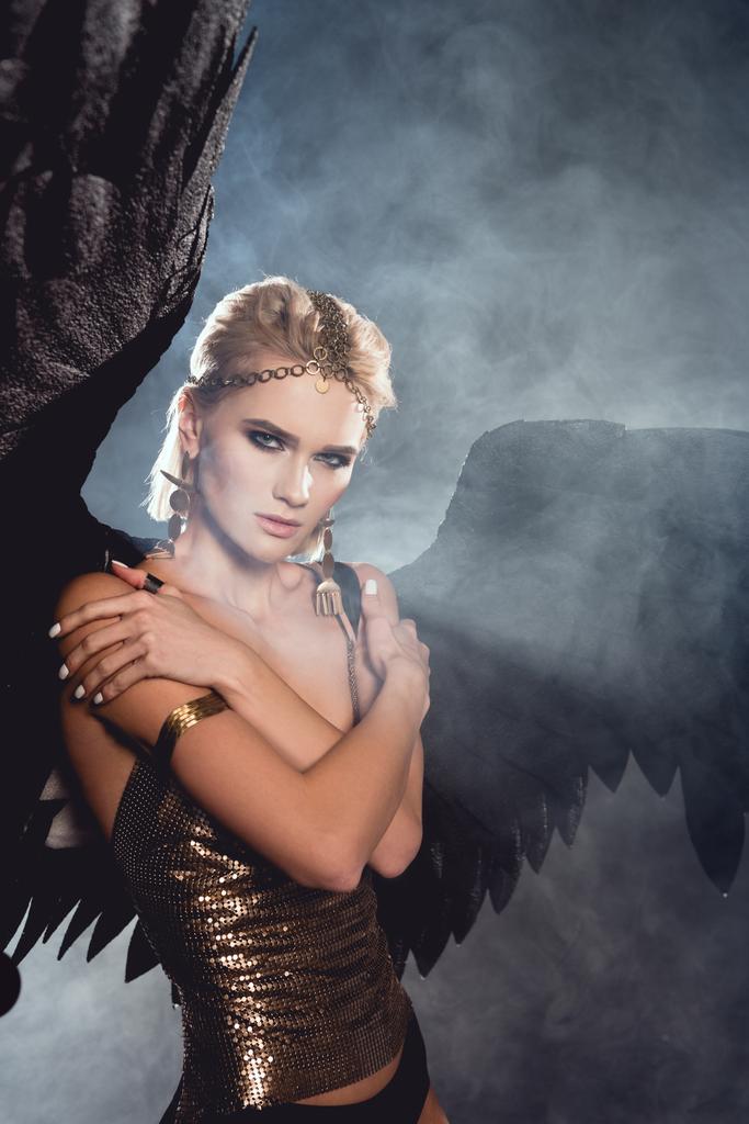 黒天使の羽と黄金アクセサリー暗い煙のような背景でポーズ美しい若いセクシーな女性 ロイヤリティフリー写真 画像素材