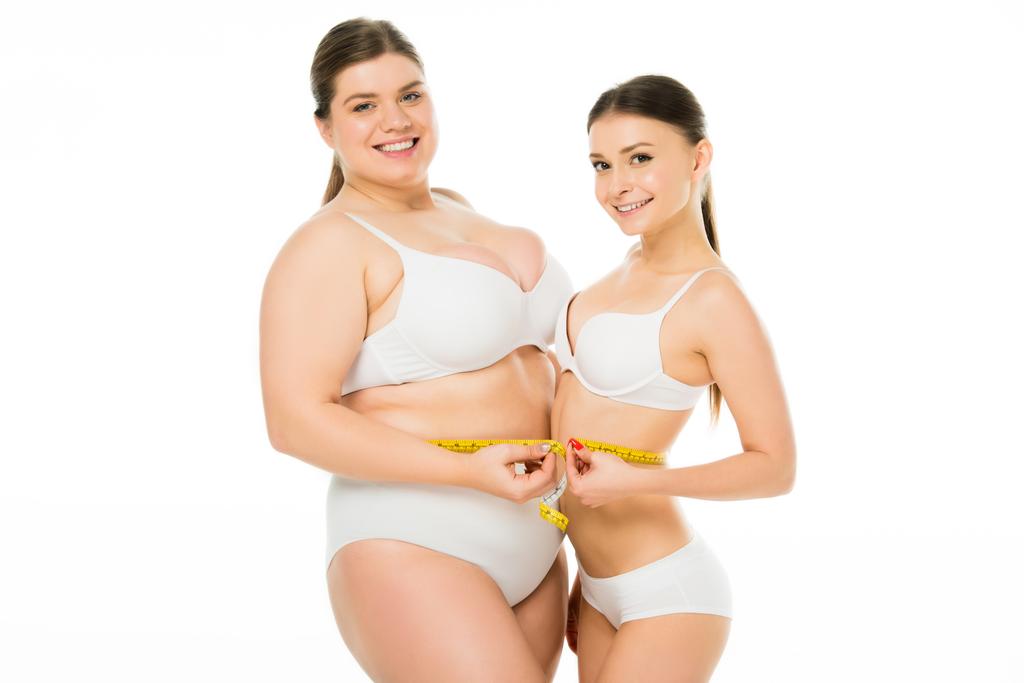 幸せボディの肯定的な肥満女性と一緒に測定テープを保持しているスリムな女性は 白で隔離 ロイヤリティフリー写真 画像素材