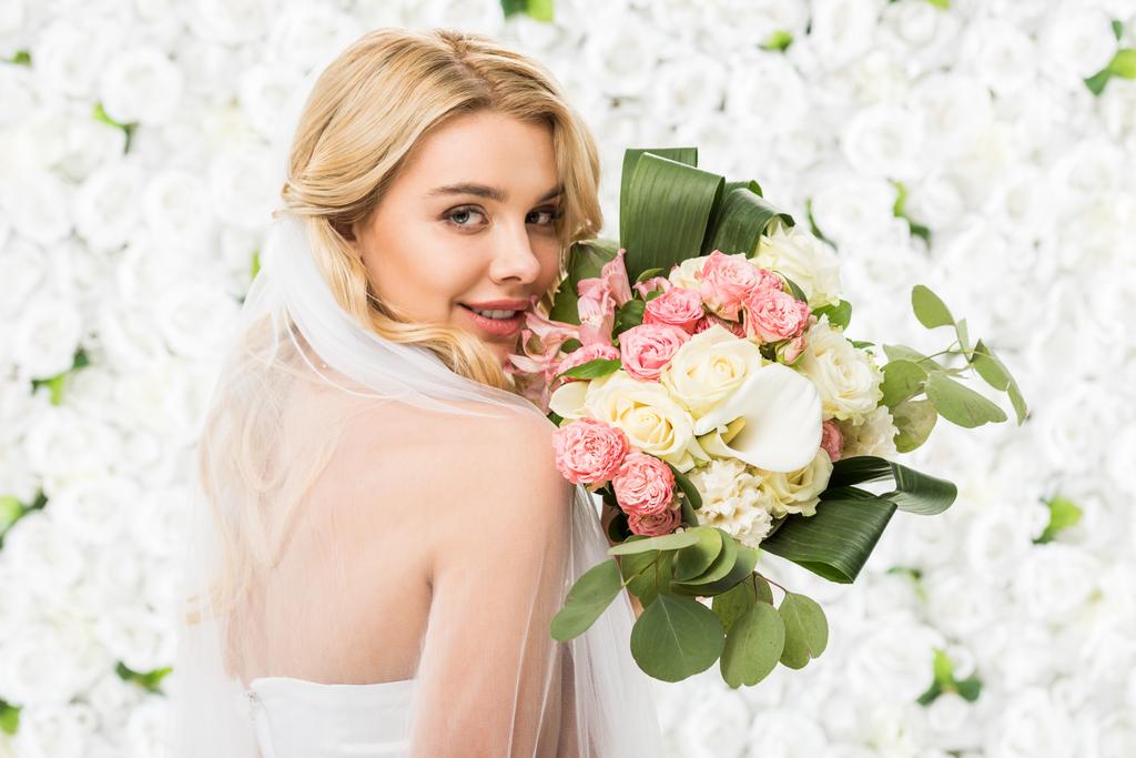 白い花の背景にウェディング ブーケを持って笑顔の魅力的な花嫁 ロイヤリティフリー写真 画像素材