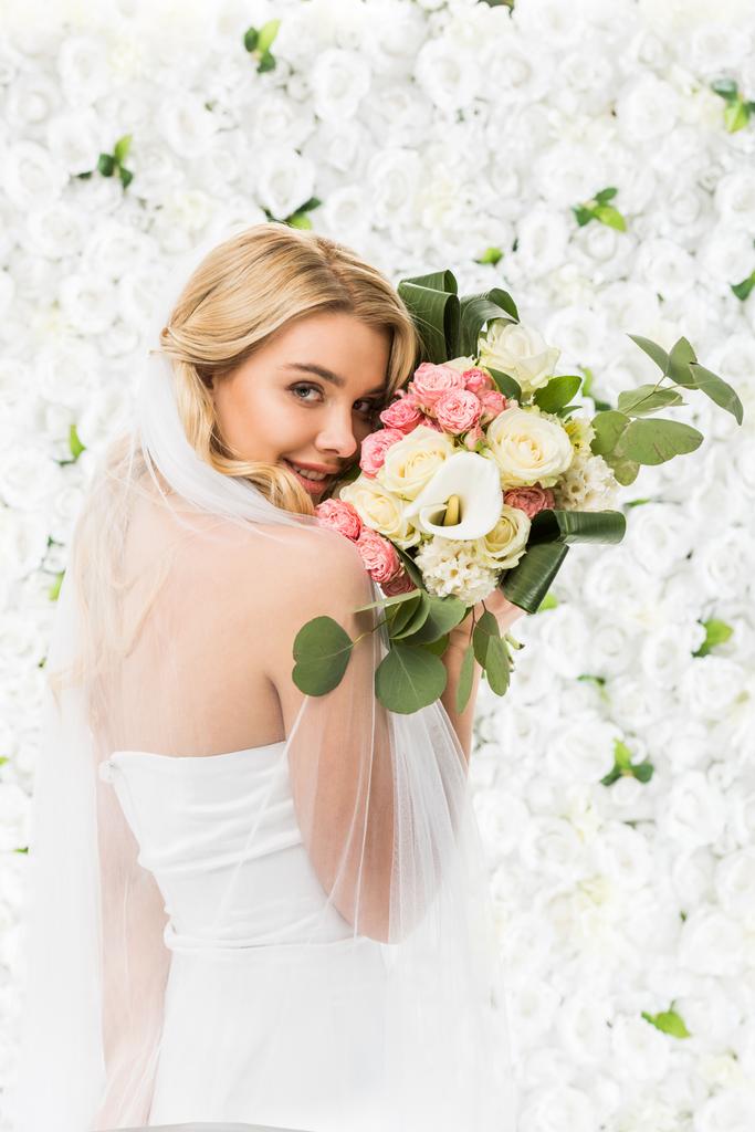 白い花の背景に顔の近くのウェディング ブーケを保持している美しい若い花嫁 ロイヤリティフリー写真 画像素材