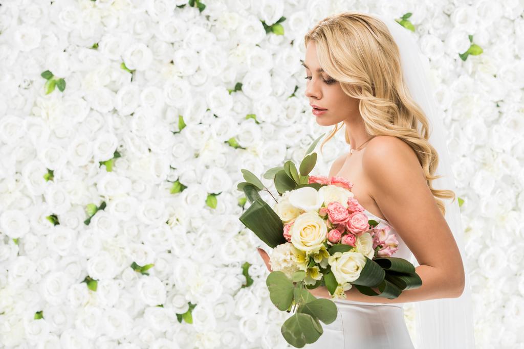 白い花の背景にウェディング ブーケを保持している美しい若い花嫁 ロイヤリティフリー写真 画像素材