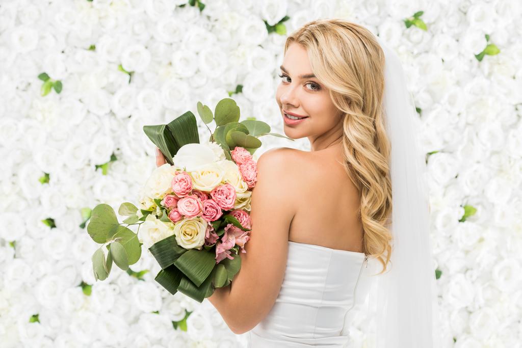 美しい若い花嫁ウェディング ブーケを押しながら白い花の背景にカメラ目線 ロイヤリティフリー写真 画像素材