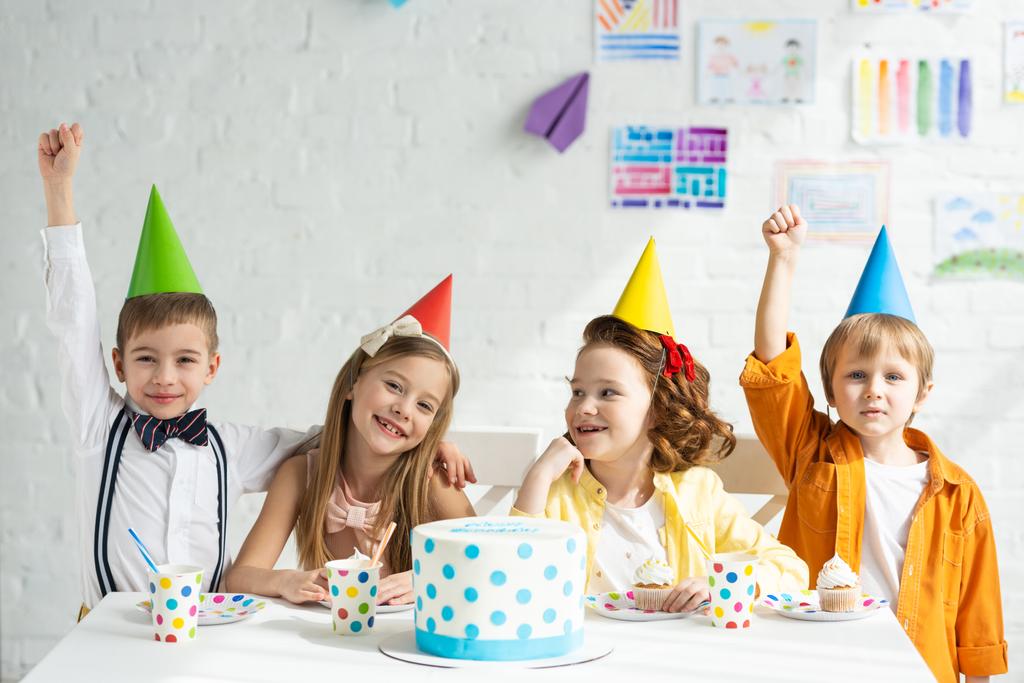 ケーキとテーブルに座って一緒に誕生日を祝うパーティーの帽子で幸せな子供たち ロイヤリティフリー写真 画像素材