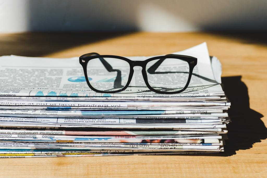Διαφορετικές εφημερίδες εκτύπωσης σε στοίβα σε ξύλινο τραπέζι με γυαλιά  Royalty-free Φωτογραφίες και Εικόνες