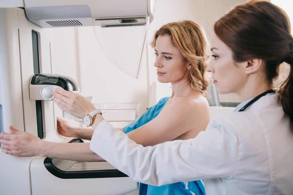 attentive-radiographer-adjusting-x-ray-machine-for-mammography-test-while-standing-near-patient