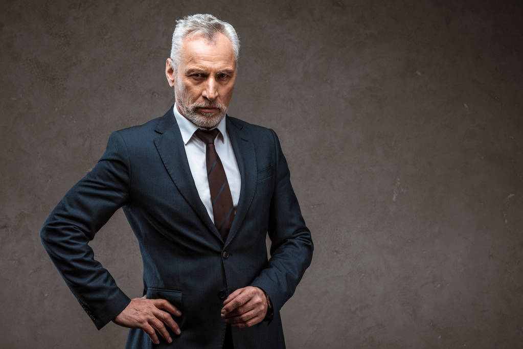灰色の腰に手を当てて立っているスーツを着た自信のあるビジネスマン ロイヤリティフリー写真 画像素材