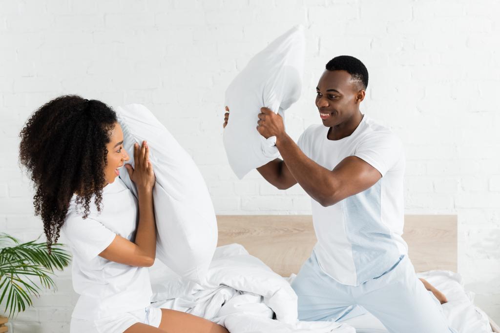 手に枕でベッドの上で戦うアフリカ系アメリカ人のカップル ロイヤリティフリー写真 画像素材