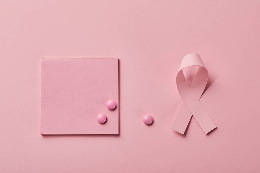 薄いピンクの背景に乳がんのリボンの近くの紙の上に散乱錠剤 ロイヤリティフリー写真 画像素材