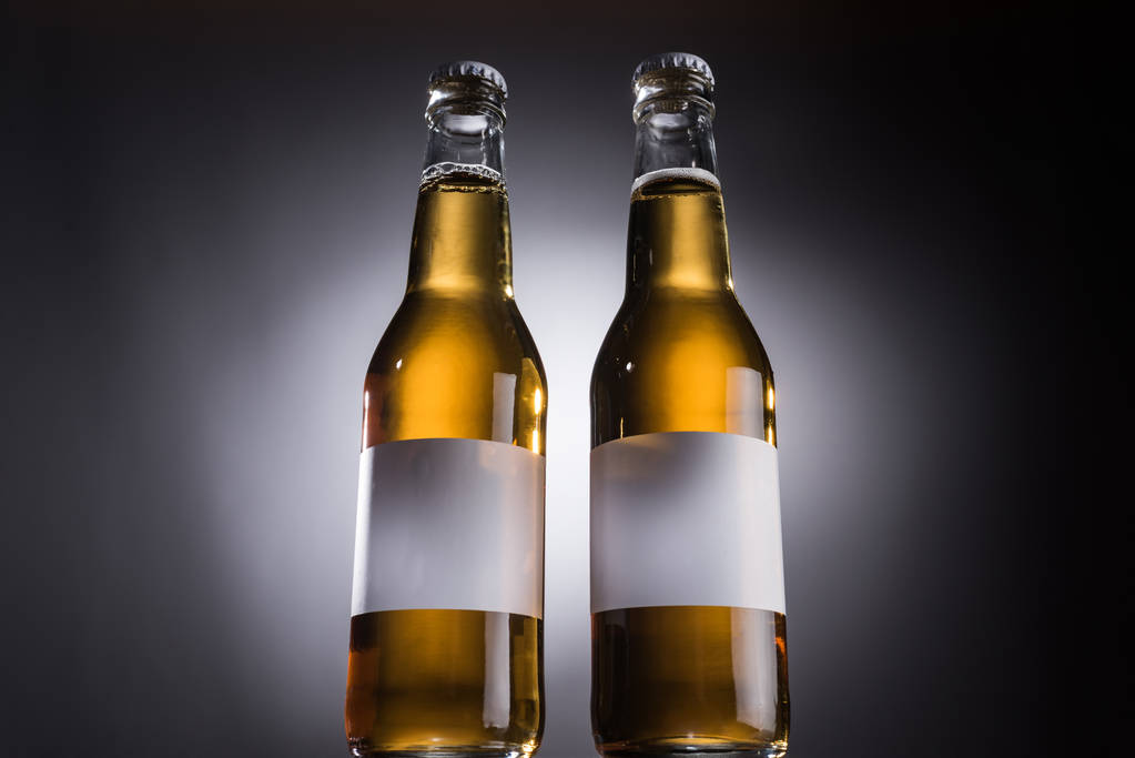 バックライト付き暗い背景にビールとラベルを持つ2つのガラスボトルの低角度ビュー ロイヤリティフリー写真 画像素材