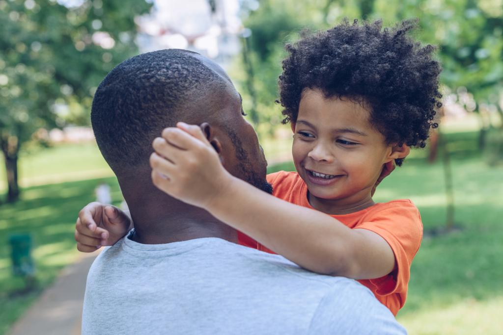 Download Cute African American Boy Hugging Father While Walking In Park Free Stock Photo And Image