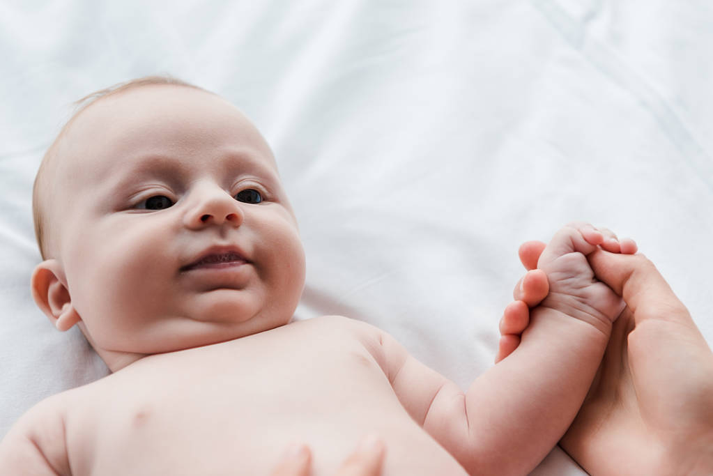 ベッドの上で可愛い赤ちゃんの娘の手を握っている母親の ロイヤリティフリー写真 画像素材