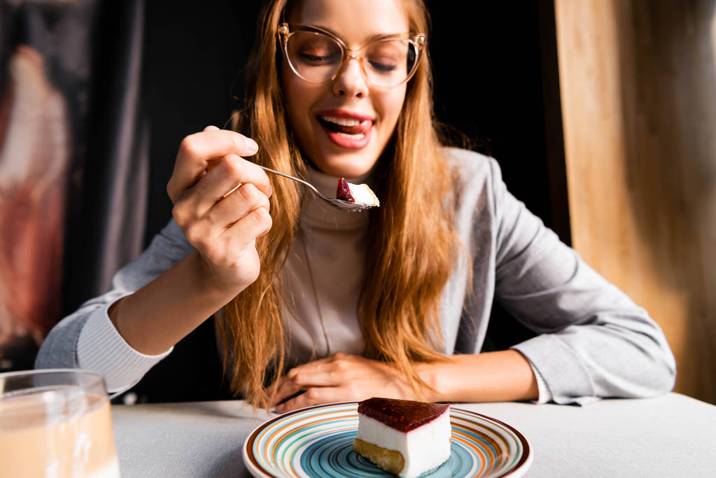 カフェでコーヒーとおいしいケーキを食べながら舌を出している魅力的な女の子 ロイヤリティフリー写真 画像素材