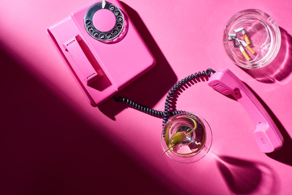 ピンク色の表面にタバコの吸い殻で迷い横にカクテルやレトロな電話のトップビュー ロイヤリティフリー写真 画像素材