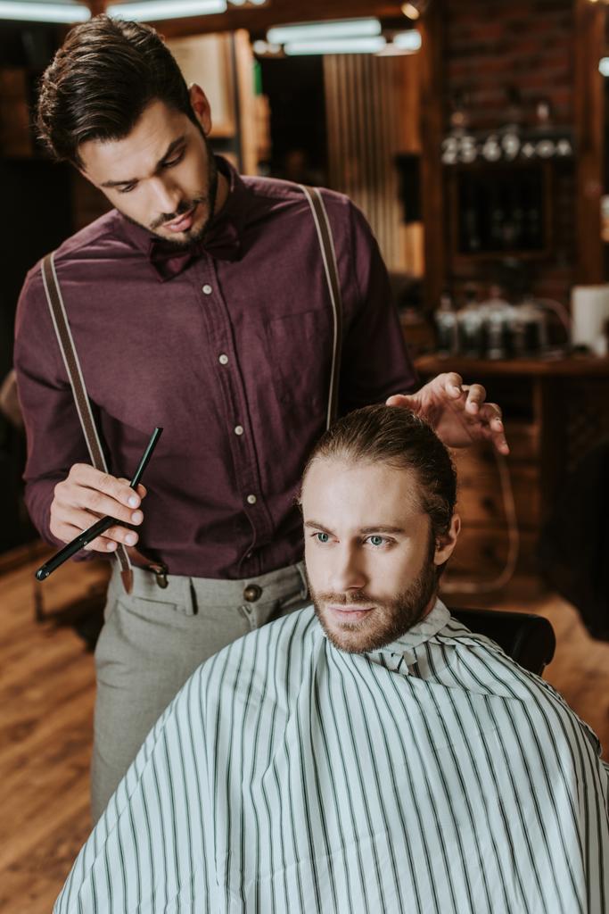 理髪店の髭の男の近くに立って剃刀を持っているスタイリッシュな理髪店 ロイヤリティフリー写真 画像素材