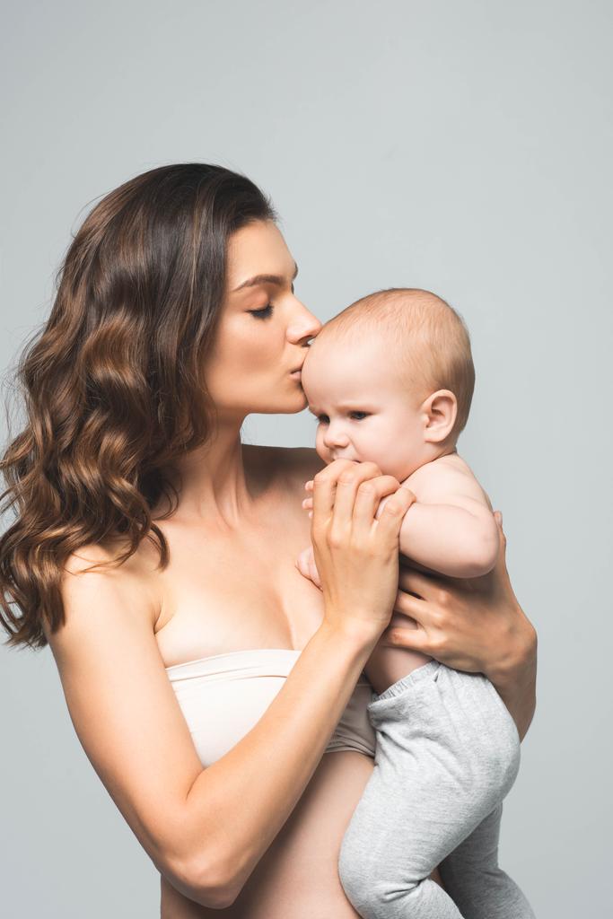 魅力的な母親の肖像画灰色で隔離された赤ん坊の少年にキス ロイヤリティフリー写真 画像素材