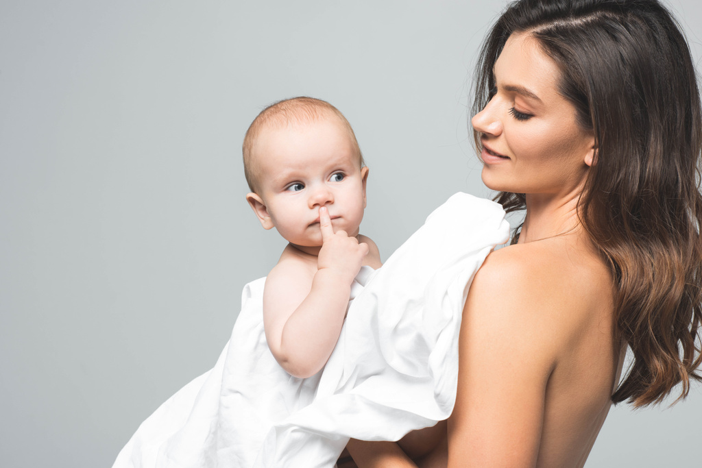 幸せな裸の母親の肖像画面白い赤ちゃんを抱きかかえて 灰色で隔離された ロイヤリティフリー写真 画像素材
