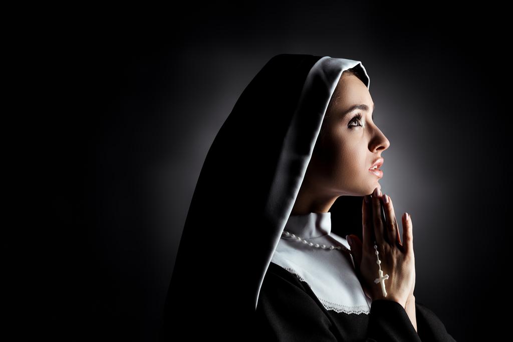 灰色の十字架で祈りながら上を見上げる美しい若い修道女 ロイヤリティフリー写真 画像素材