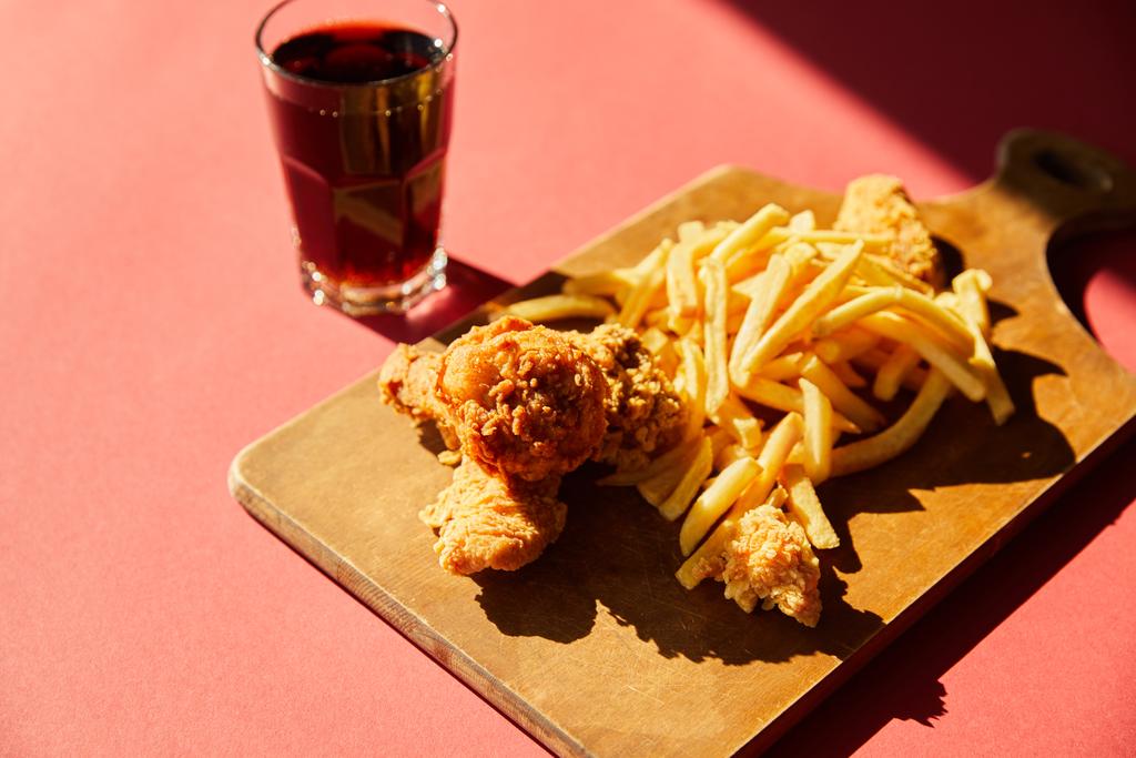 Download Crispy Deep Fried Chicken And French Fries Served On Wooden Cutting Board With Soda In Sunlight Free Stock Photo And Image