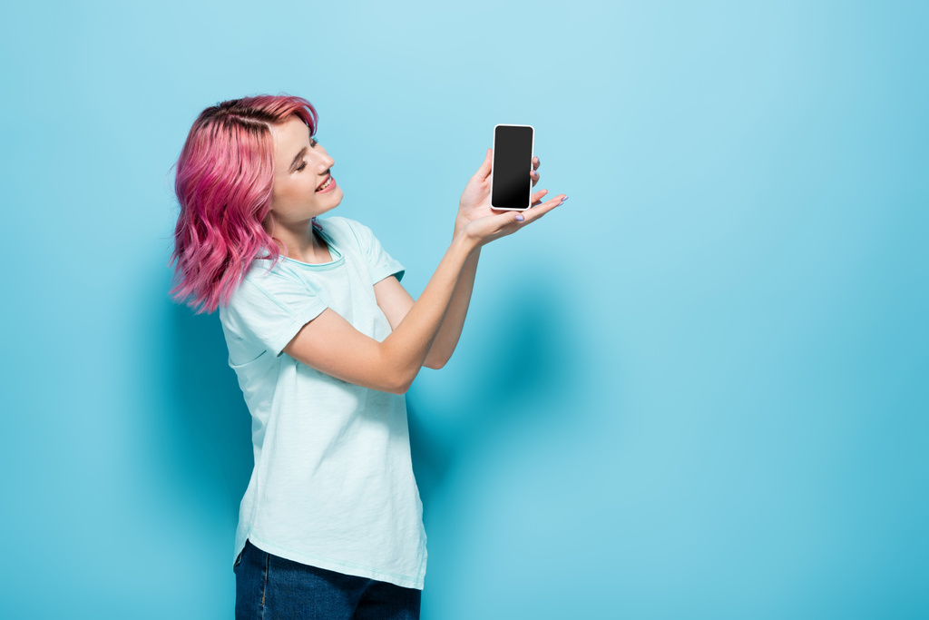 青い背景に青い画面のスマホを持っているピンクの髪の若い女性 ロイヤリティフリー写真 画像素材