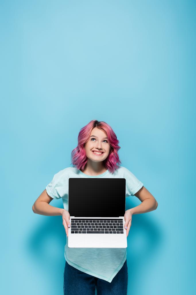 ピンクの髪をした若い女性が黒い画面でノートパソコンを見せ青い背景を見上げ ロイヤリティフリー写真 画像素材