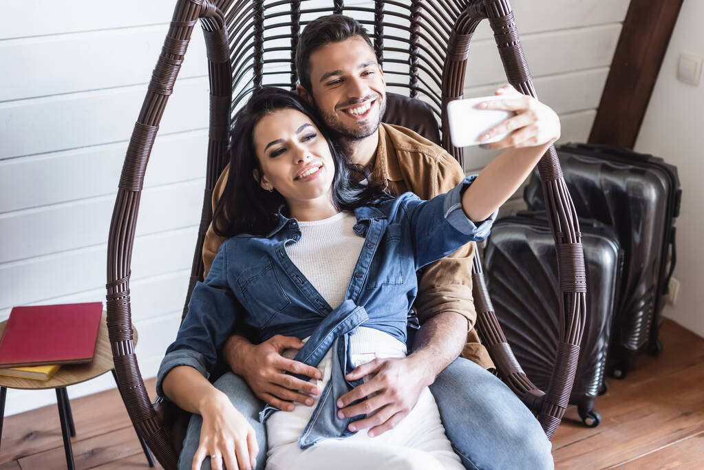 陽気なカップルが籐製の椅子に腰掛けながらスマホで自撮り ロイヤリティフリー写真 画像素材