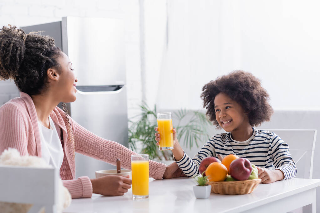 アフリカ系アメリカ人の女の子が朝食中に母親の近くでオレンジジュースを持っていて ロイヤリティフリー写真 画像素材