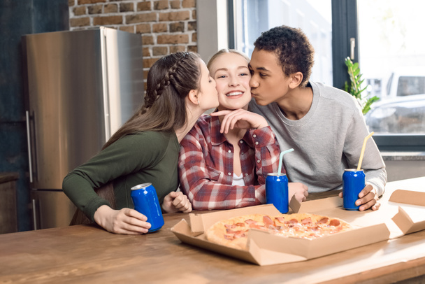 ホーム コンセプトでピザを食べて 10 代の少女の頬に笑みを浮かべてキス友人の側面図 ロイヤリティフリー写真 画像素材