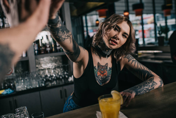 cropped image of tattooed bartender giving high five to visitor at bar - Ph...
