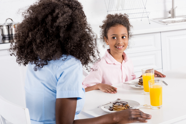 幸せなアフリカ系アメリカ人家族ダイニング ルームで朝食にパンケーキとオレンジ ジュースを使用 ロイヤリティフリー写真 画像素材