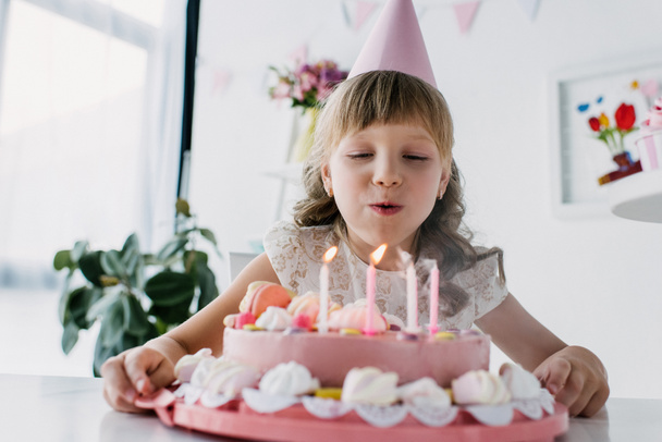 バースデー ケーキのろうそくを吹きコーンで幸せなかわいい子供 ロイヤリティフリー写真 画像素材